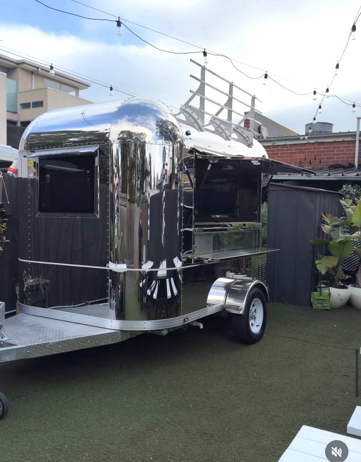 Polished stainless steel Airstream-style food trailer with serving window open, string lights overhead