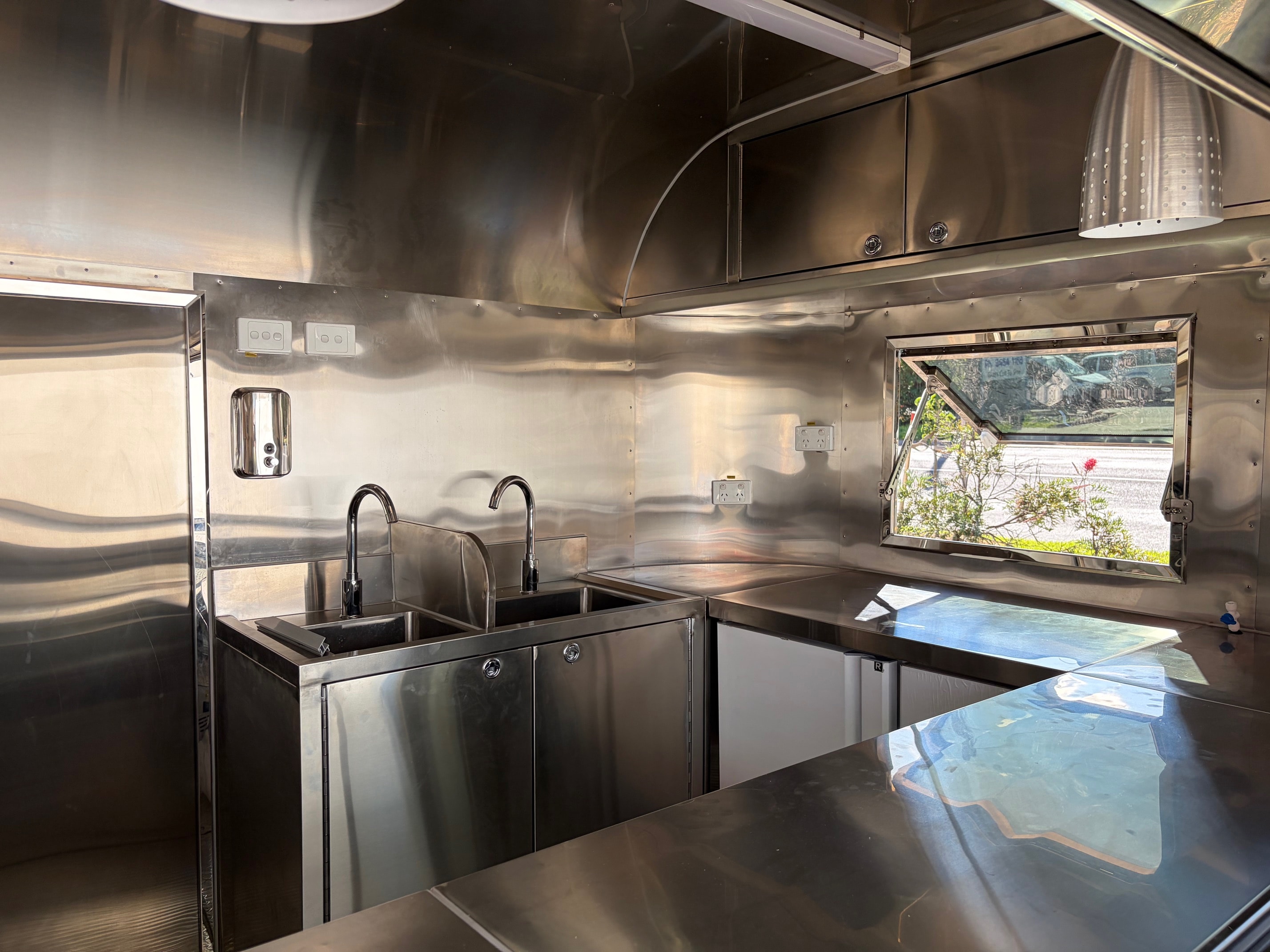 Stainless steel commercial kitchen interior of Airstream trailer with dual sinks and overhead cabinetry