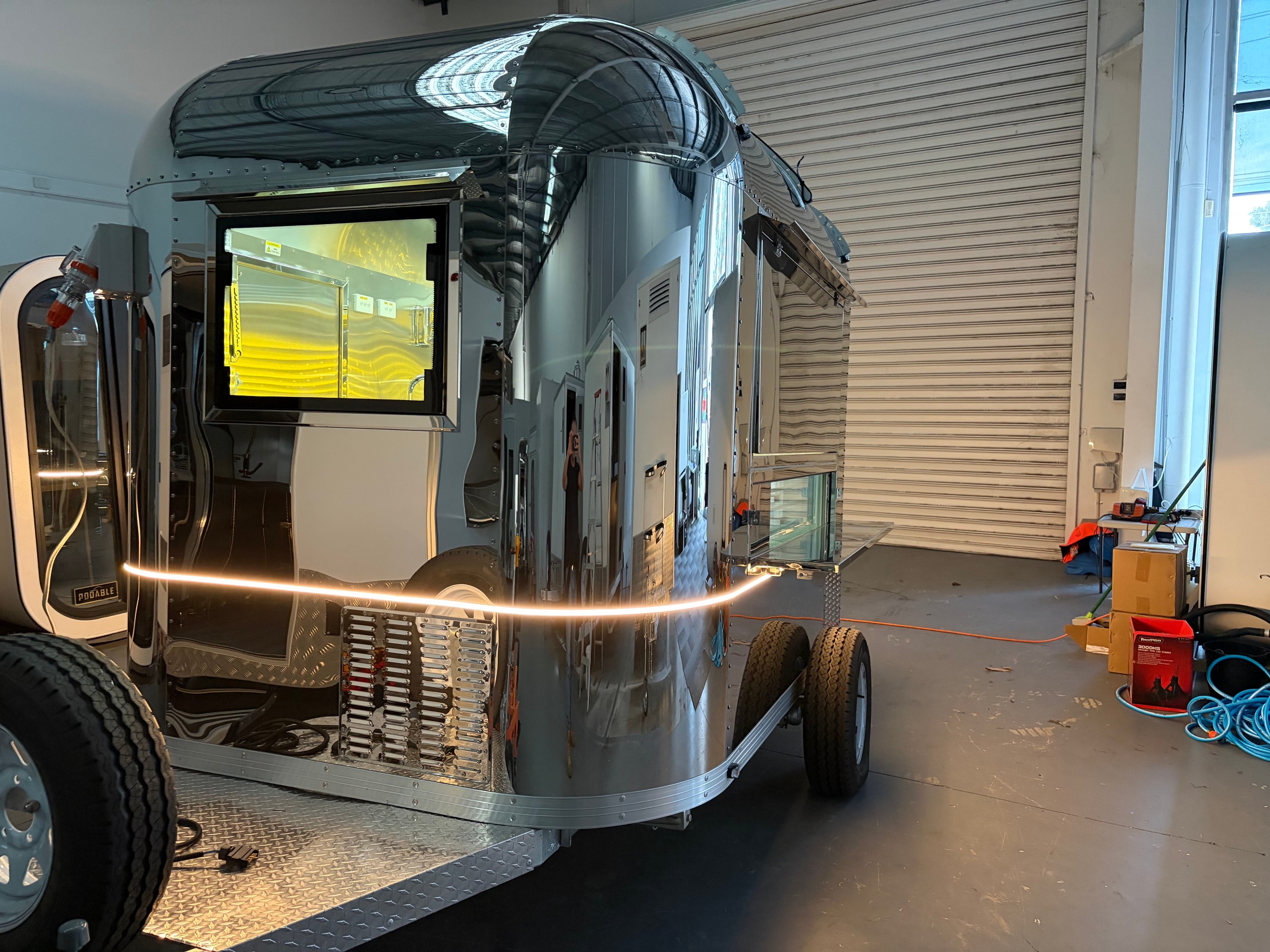 Mirror-polished Airstream food trailer in workshop with LED accent strip and display screen