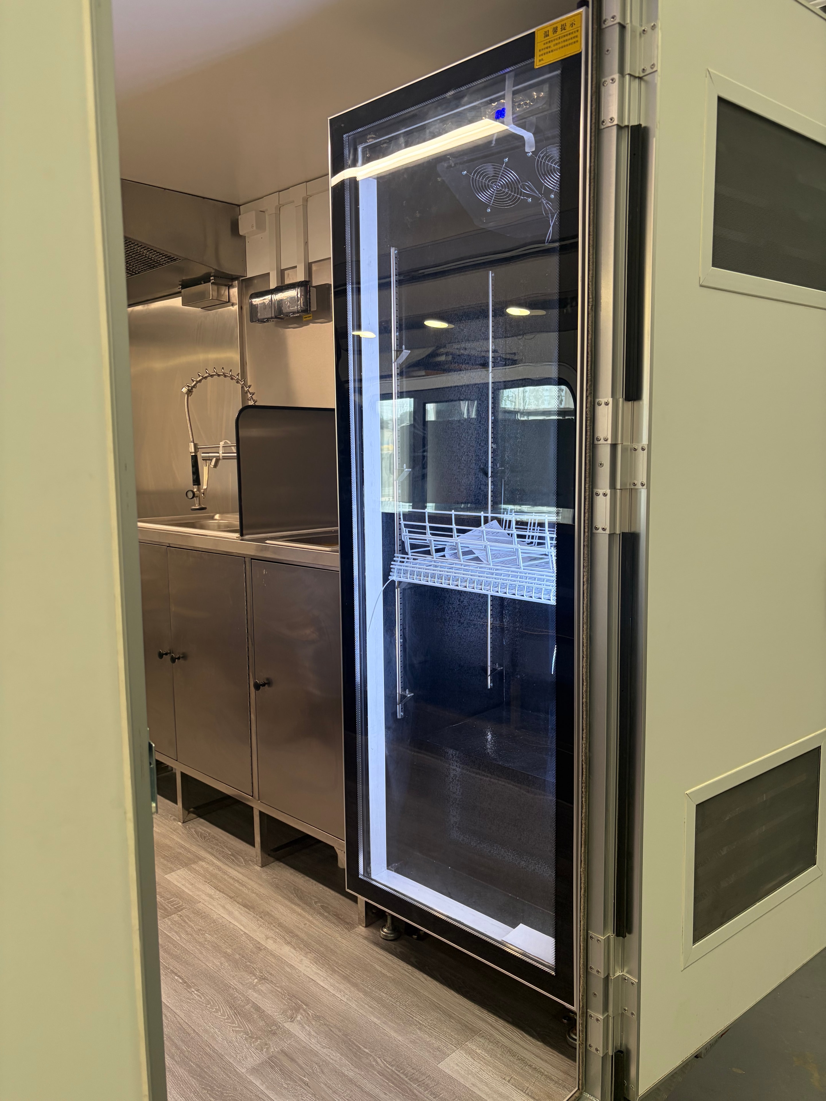 Interior of food trailer showing display fridge with glass door and stainless steel benches