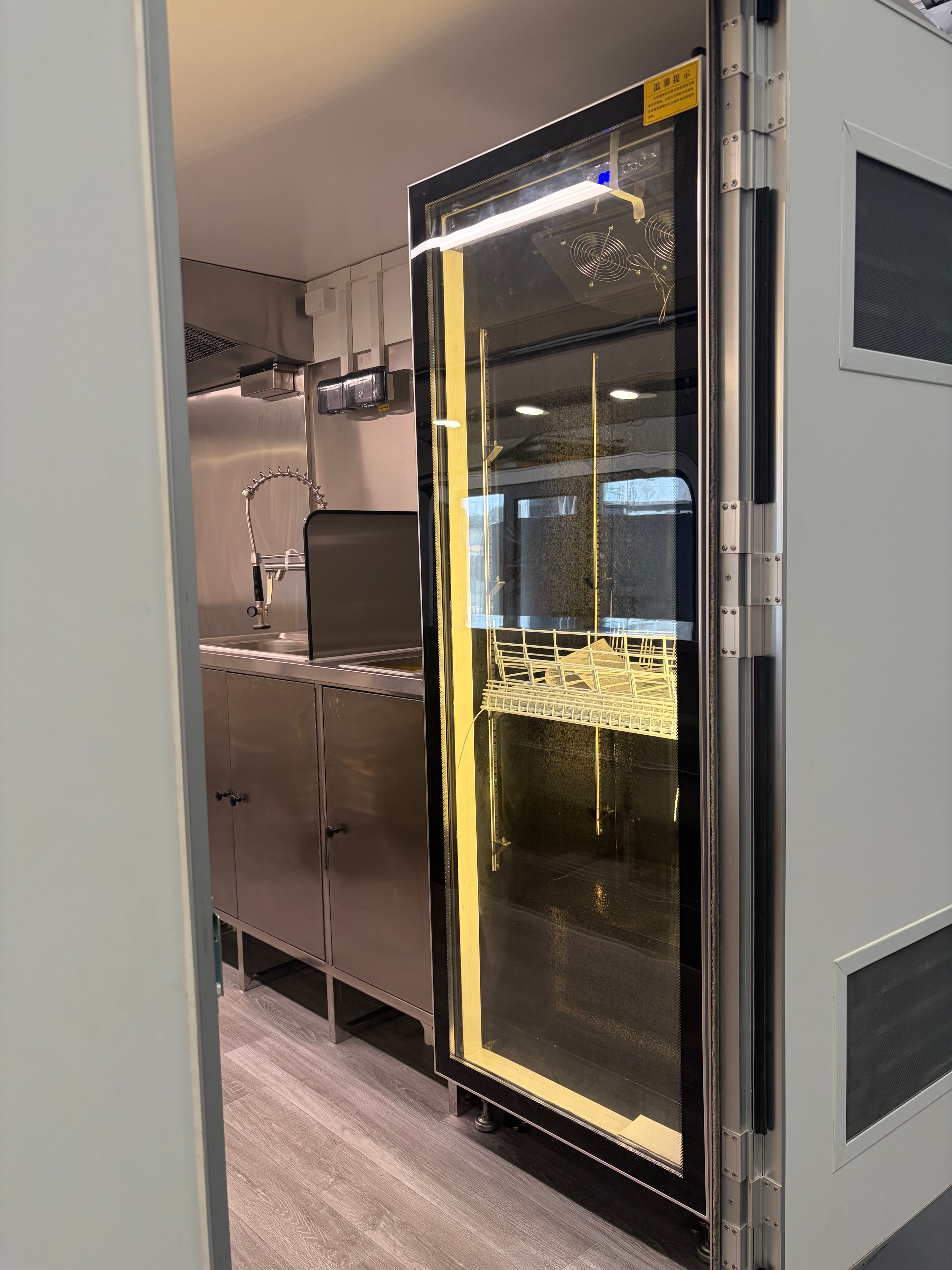 Interior display fridge with yellow-tinted lighting and stainless steel kitchen fitout